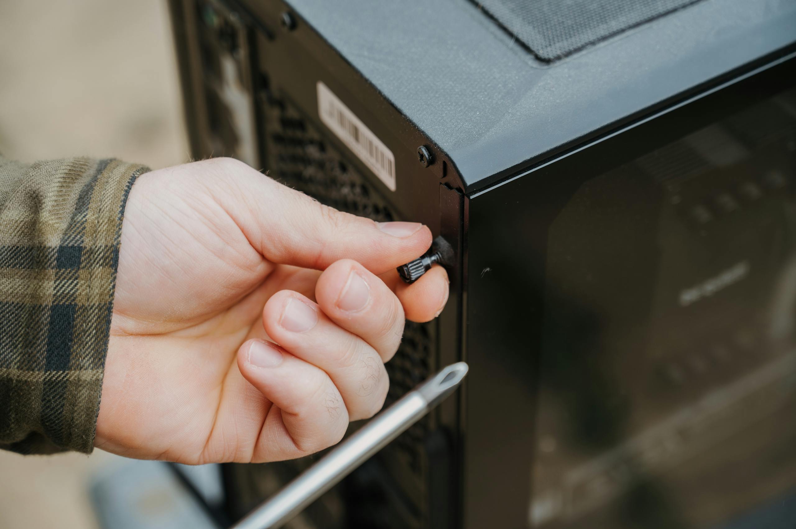 Close-up of a hand unscrewing a desktop computer case, emphasizing technology maintenance.